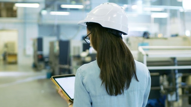 戴安全帽的美丽女工业工程师在大工厂里使用平板电脑。视频素材