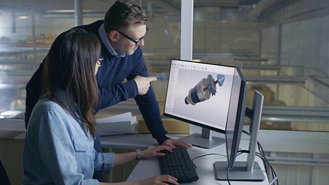 女性工业工程师和男性项目经理在她的CAD软件三维涡轮/发动机模型。从办公室的窗户可以看到工厂的内部。视频素材
