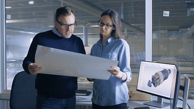 女性工业工程师和男性总工程师与蓝图工作。桌面电脑显示3D涡轮/发动机模型。视频素材