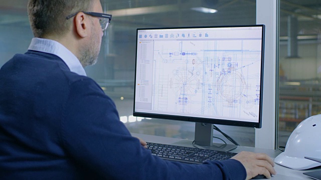 一名男性工业工程师在电脑上绘制技术蓝图。从她办公室的窗户可以看到工厂里面。视频素材