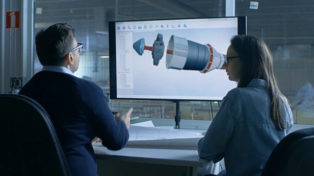 男性和女性工程师工作与蓝图，而演示显示显示3D模型的涡轮/引擎部件。在背景中可以看到功能植物。视频素材