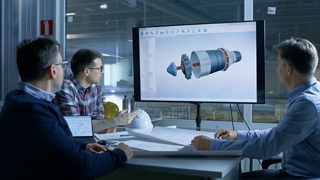 工业工程师小组讨论三维模型的涡轮/发动机设计显示在演示显示。在背景工厂被看到。视频下载
