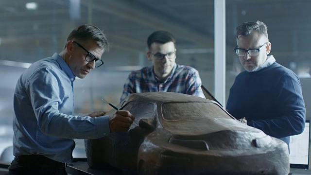 汽车设计工程师小组讨论新的橡皮泥原型模型。他们在一家大型汽车厂工作。视频下载