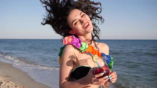 肖像女孩在夏天的海滩上，美丽的卷发看着相机在海边拿着鸡尾酒，性感的年轻女人视频素材