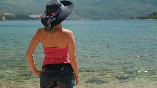 一个年轻女子站在阳光灿烂的下午的海滩上视频素材