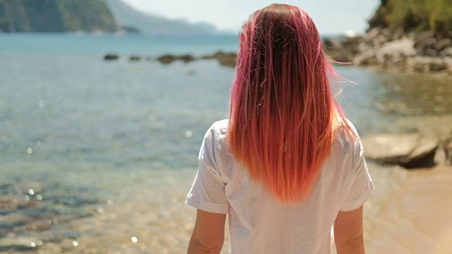 一个美丽的女人半转身的肖像，粉红色的头发在海滩上视频素材