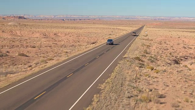 航拍:黑色汽车行驶在空旷的路上，穿过无尽的沙漠山谷视频下载