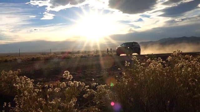 慢镜头:金色的日出，黑色的SUV行驶在尘土飞扬的砾石路上视频下载