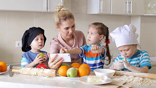 年轻女子在厨房做饭，一边在手机上看菜谱。孩子们帮助妈妈做饭视频素材