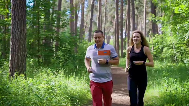朋友们过着积极的生活方式，在公园的乡间小路上跑步，一男一女穿着运动服在运动中聊天视频素材