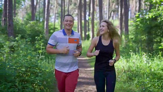 一对穿着运动服的年轻夫妇在一个阳光明媚的日子里跑过森林，一位女运动员问一位男士他们已经跑了多远视频素材