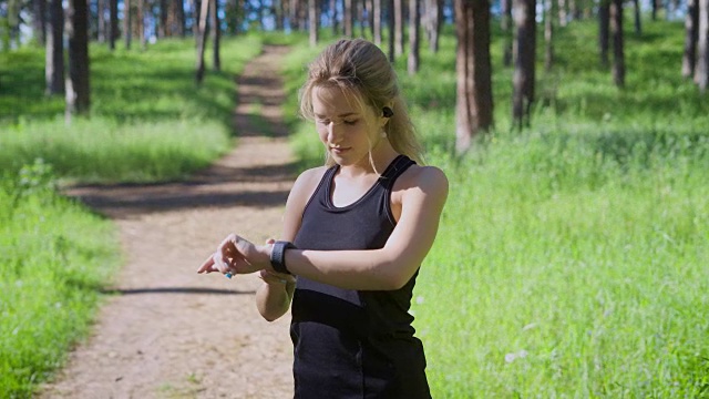 一个年轻的金发女人改变智能手表上的设置，一个跑步的运动员想知道她跑了多少公里视频素材