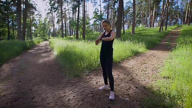 一名年轻女子把一个智能手表戴在手上，以便知道她在一个温暖的夏天穿过公园跑了多少公里视频素材