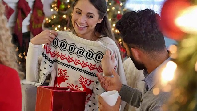 快乐的年轻女子打开圣诞礼物在丑陋的圣诞毛衣礼物交换视频下载