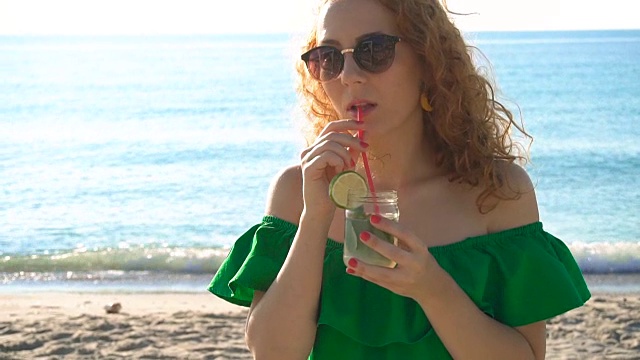 年轻女子在海边享用热带莫吉托鸡尾酒和新鲜的酸橙视频素材