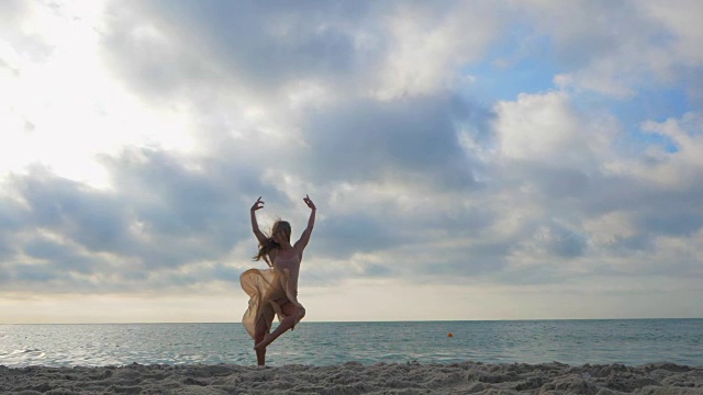在日出或日落的米色丝绸连衣裙和尖在海边的沙滩上跳芭蕾舞者。剪影的年轻美丽的金发女人长头发练习拉伸和经典的练习。史诗般的跳。慢动作视频素材