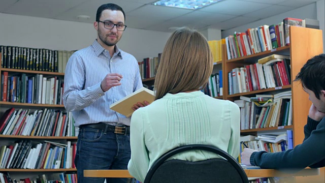 年轻男老师拿着书在图书馆与学生交谈视频素材
