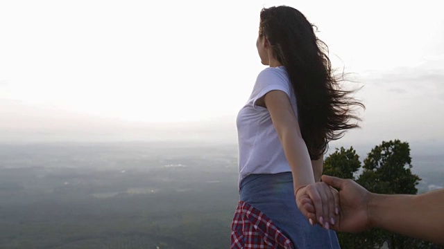 女孩牵着男人的手在山顶，幸福的微笑，夫妇欣赏早晨的风景视频素材