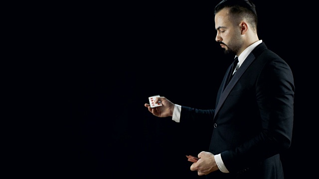 专业熟练的魔术师在黑色的西装表演卡消失和出现把戏多次。背景是黑色的。视频下载