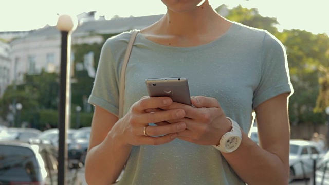一个穿着蓝色t恤的年轻女子正在夏天的城市里使用手机。特写,慢动作。视频素材