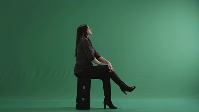 一个女人双腿交叉坐在手提箱上视频素材