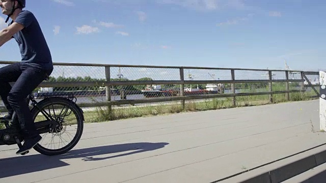 英俊的男人骑着黑色的载货自行车沿河而行视频素材