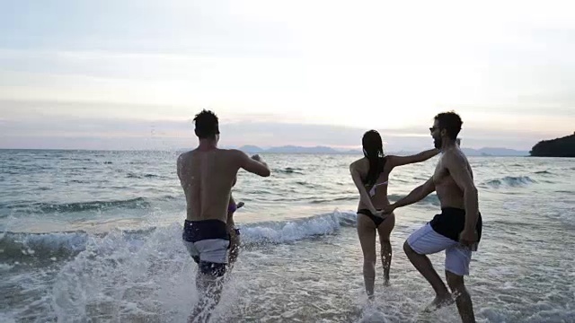 两对夫妇在海中跑步使水花手，朋友群在海滩在日落有乐趣视频素材