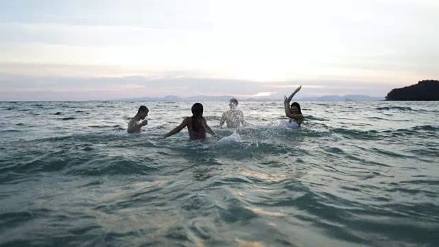 一群朋友在海边游泳在日落年轻人在水里嬉戏在海滩上视频素材