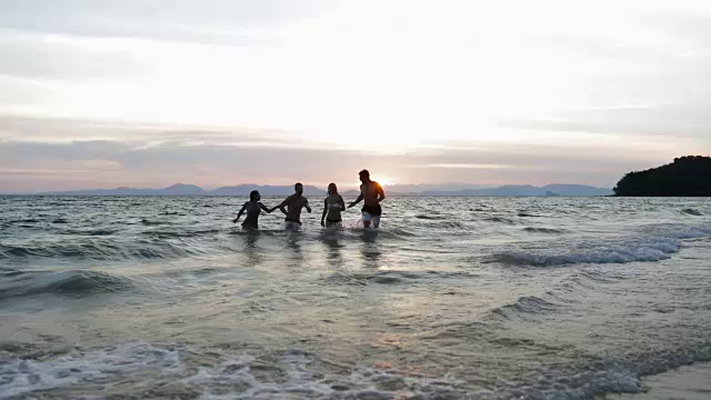一群人从海边跑在日落，快乐的年轻朋友一起在海滩上度过暑假视频素材