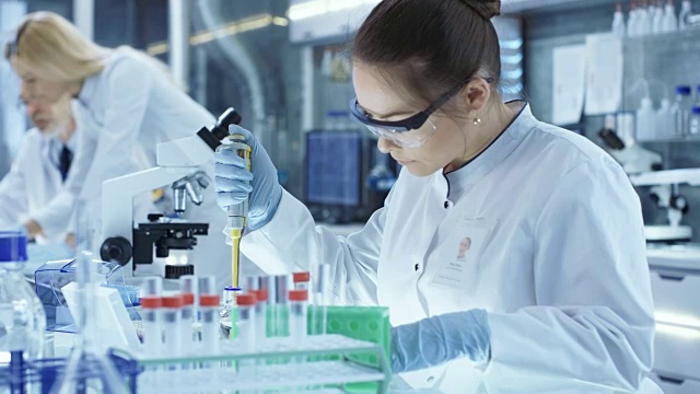 女研究科学家在一个大的现代实验室使用微型管填充试管。在背景中，科学家正在工作。视频素材