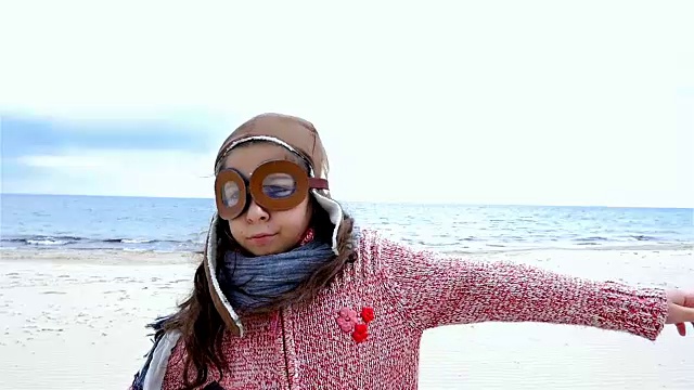 小女孩戴着飞行员帽，像一架飞机在蓝天下张开双臂，慢镜头视频素材