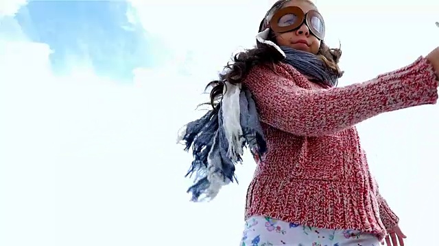 小女孩戴着飞行员帽在蓝天下玩木制飞机，慢镜头视频素材