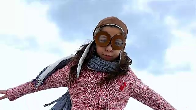 小女孩戴着飞行员帽，像一架飞机在蓝天下张开双臂，慢镜头视频素材