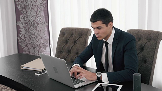 英俊的商人使用笔记本电脑，近距离的商人与笔记本电脑和平板电脑在现代办公室视频下载