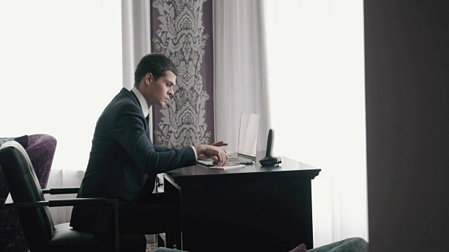 英俊的商人使用笔记本电脑，近距离的商人与笔记本电脑和平板电脑在现代办公室视频素材