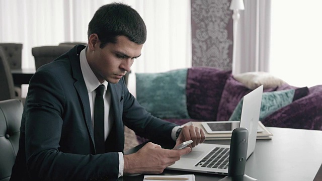 英俊的商人使用笔记本电脑，近距离的商人与笔记本电脑和平板电脑在现代办公室视频素材