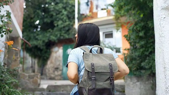 夏日里，一名年轻女子背着双肩背包漫步在古老的欧洲小镇上。视频素材