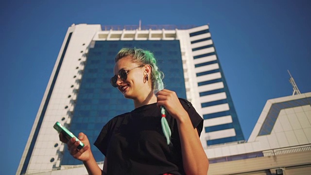 年轻时尚的潮女人与绿色头发的肖像使用智能手机在城市建筑的背景，慢动作视频素材