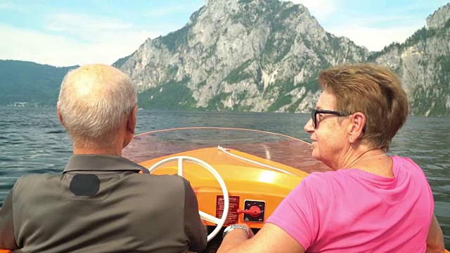 老年人在世界上，活跃的老年夫妇驾驶电动船在山湖上视频下载