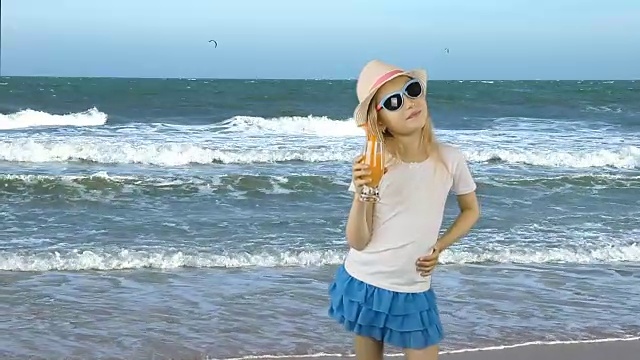 年轻的白人女孩站着，用吸管喝着橙汁鸡尾酒。海岸地平线。喝橙汁的女孩。假期。有相同的剪辑与透明背景阿尔法通道。视频素材