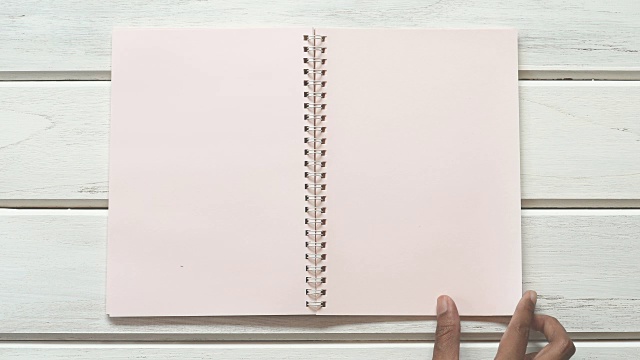 一个男手打开日记本放在白色的木桌上，俯视图和头顶拍摄使用空白模板对书本进行模拟，以添加任何文本内容视频素材