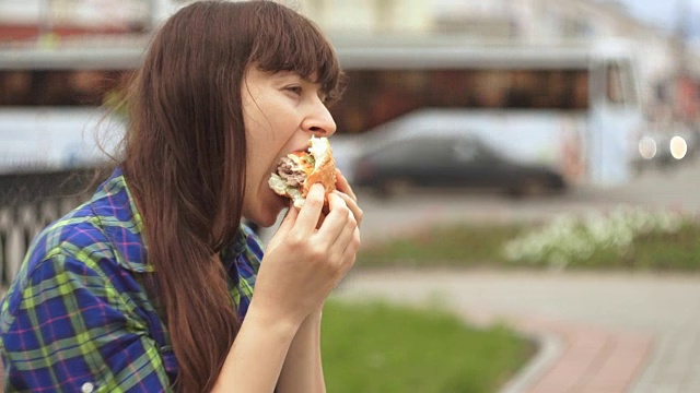 一个女人在繁忙的街道旁咬着一个汉堡的肖像视频素材