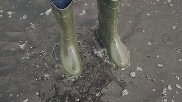 穿着胶靴跳过水坑的女人。慢动作视频下载