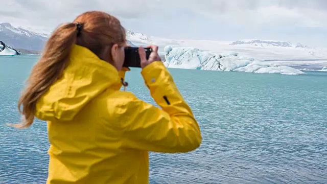 穿着黄色雨衣的女人在拍摄漂浮在水中的冰山视频下载