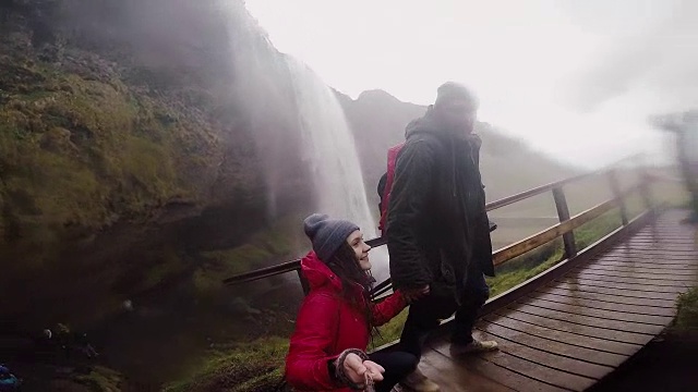 一对年轻的旅行情侣一起在冰岛的Seljalandsfoss瀑布附近散步。慢动作摄影机视频素材