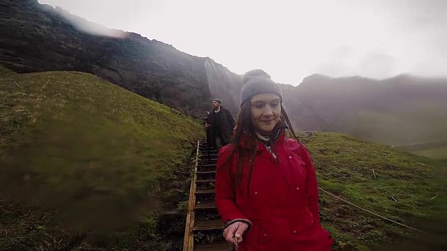 年轻快乐的女人拿着自拍杆和相机从楼梯上下来。一对夫妇在山里旅行。缓慢的莫视频素材