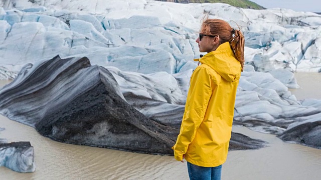 穿着黄色雨衣的女人站在冰岛冰川底部视频下载