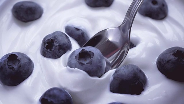 用勺子蘸奶油吃蓝莓，水果背景。4 k。视频下载