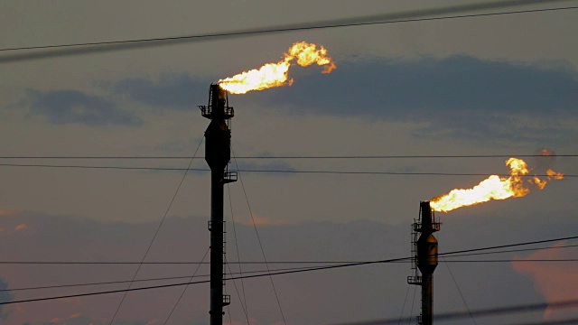 在多云的天空下，两个燃烧的火炬在炼油厂视频素材