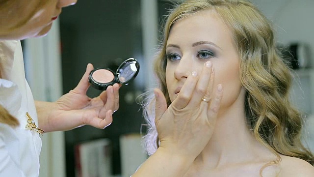 专业化妆师在年轻女子脸上涂抹化妆霜。视频素材
